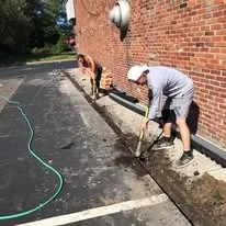 Crew preparing the ground along a brick wall for concrete work