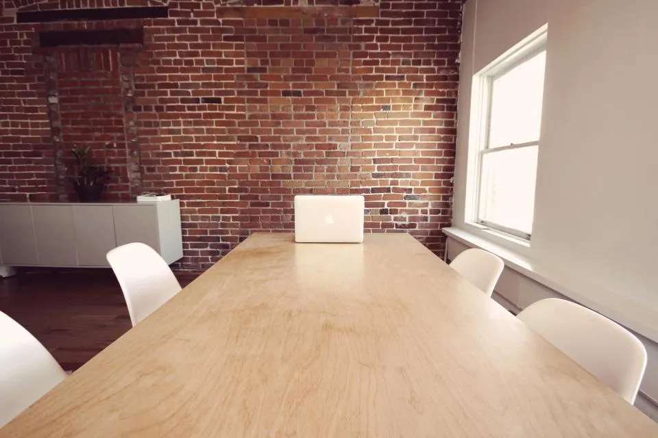 Office with a long wooden table, white chairs and a brick wall
