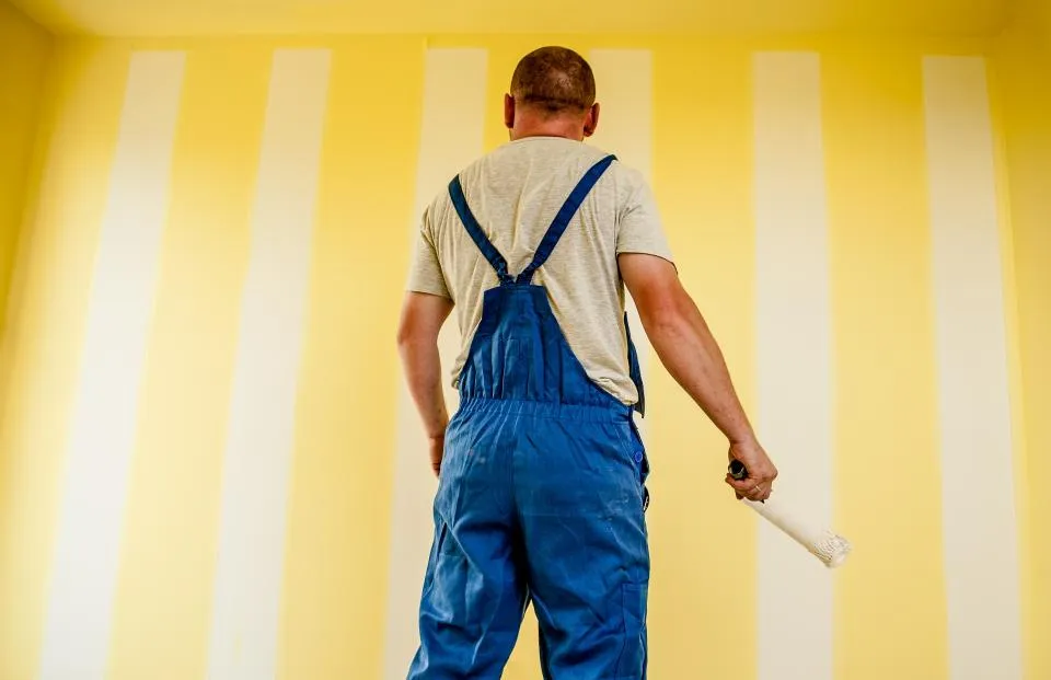 Painter in overalls painting stripes on a yellow wall