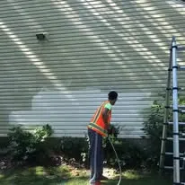 Crew member power washing green vinyl siding on a building
