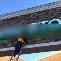 Crew member on a ladder working on a commercial storefront facade